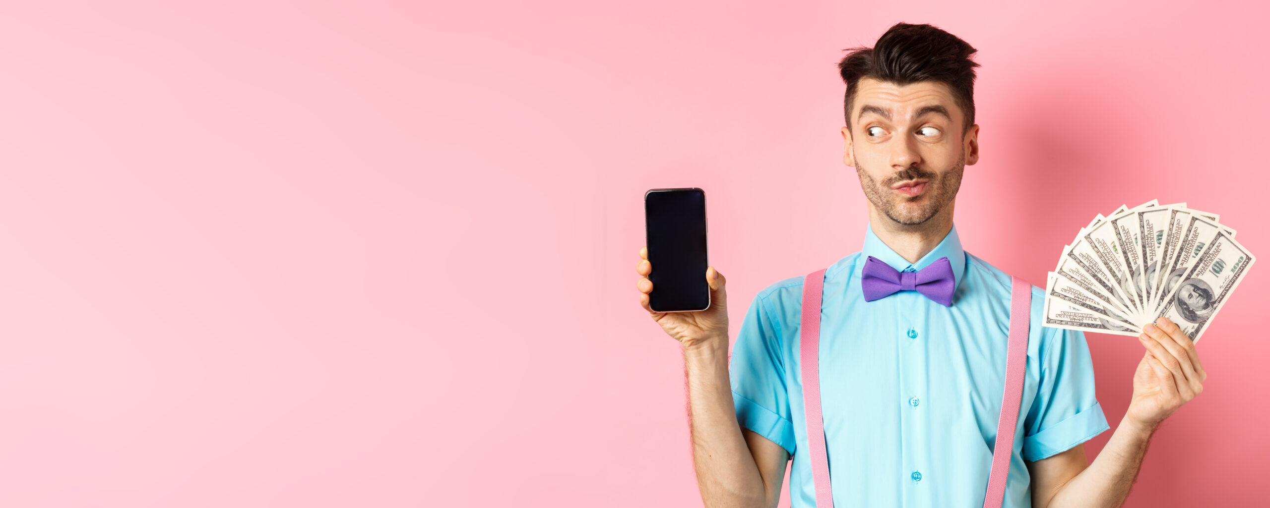 E-commerce and shopping concept. Funny guy look curious at empty smartphone screen, showing money, buying online, standing on pink background