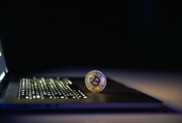 Bitcoin coin near laptop on black background. Finance and crypto money concept.