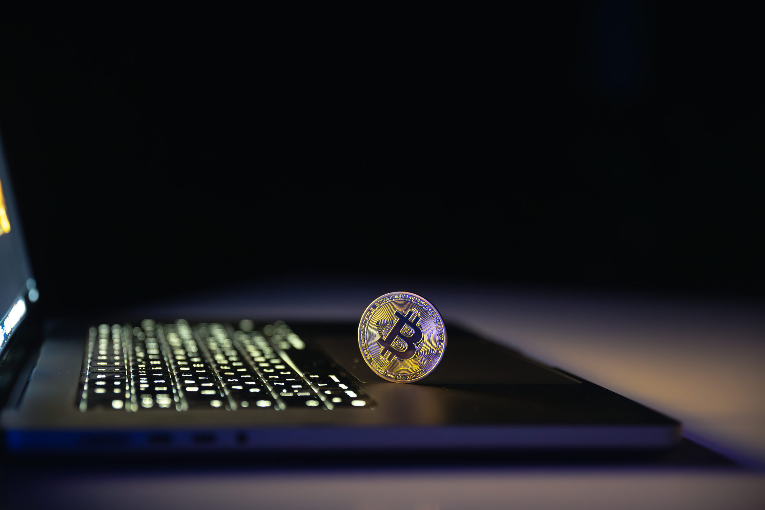 Bitcoin coin near laptop on black background. Finance and crypto money concept.